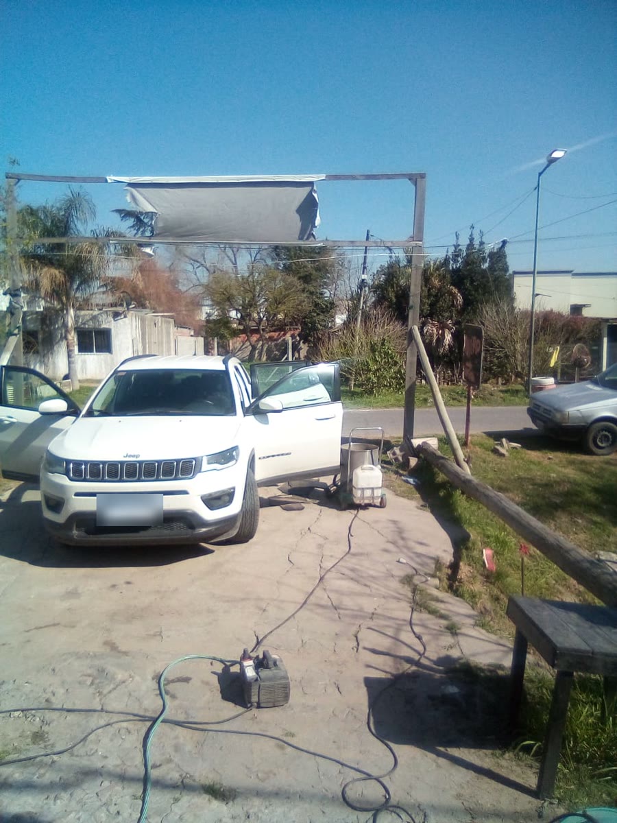 Un Jeep blanco con las puertas abiertas en el patio del lavadero, con la hidrolavadora en el piso