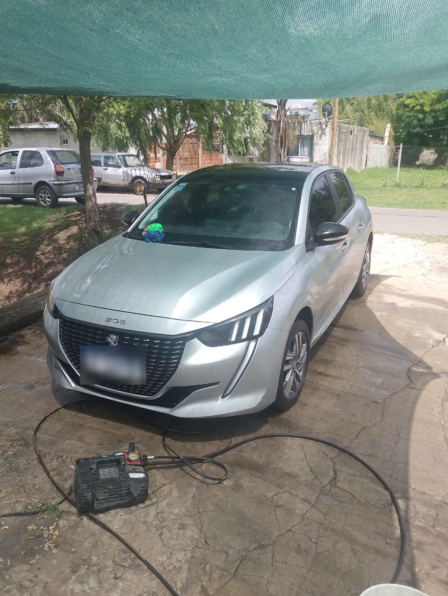 Un Peugeot 208 gris bajo la media sombra, con la hidrolavadora al lado